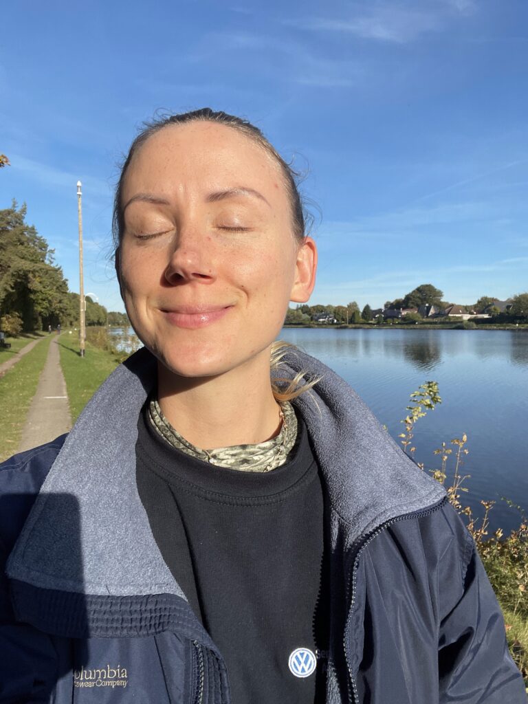 Sylwia uśmiecha się z zamkniętymi oczami ciesząc się promieniami słońca w zimny dzień na tle kanału kilońskiego w Rendsburgu, tam gdzie mieszka.